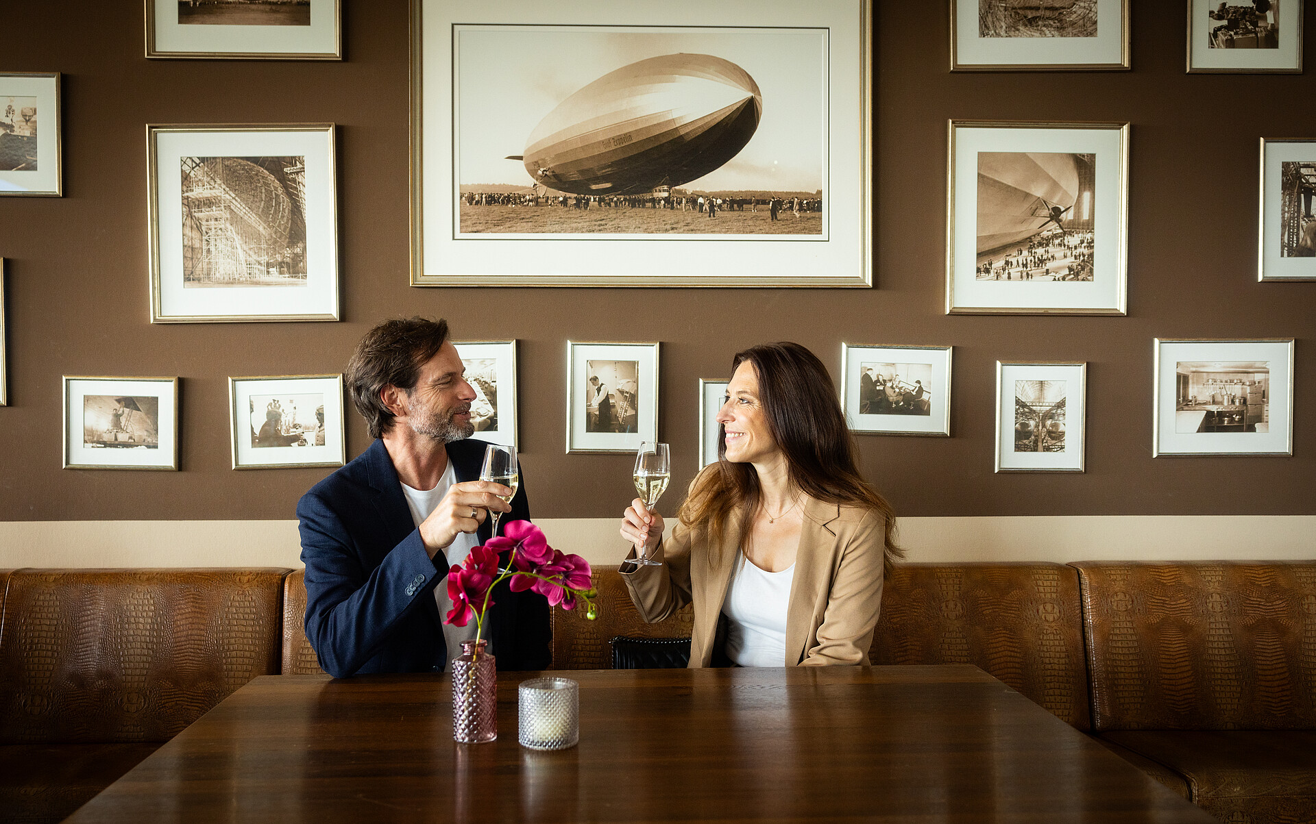 Paar sitzt im Zeppelin-Hangar-Restaurant und stößt mit einem Glas Sekt an